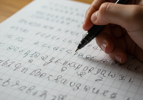 Hand practicing cursive alphabet on a lined paper sheet.
