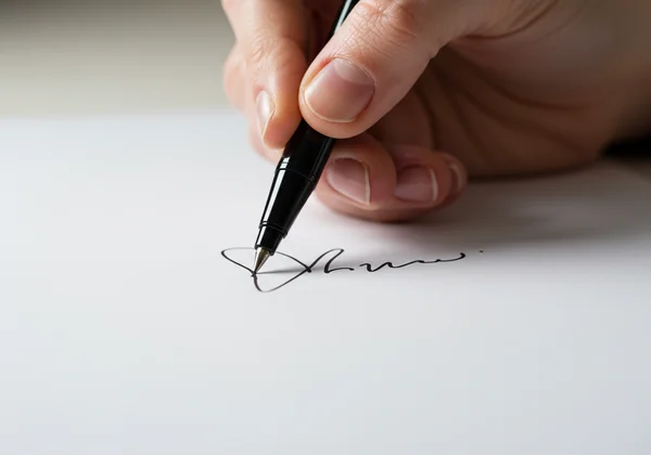 Hand writing an elegant cursive signature on paper.